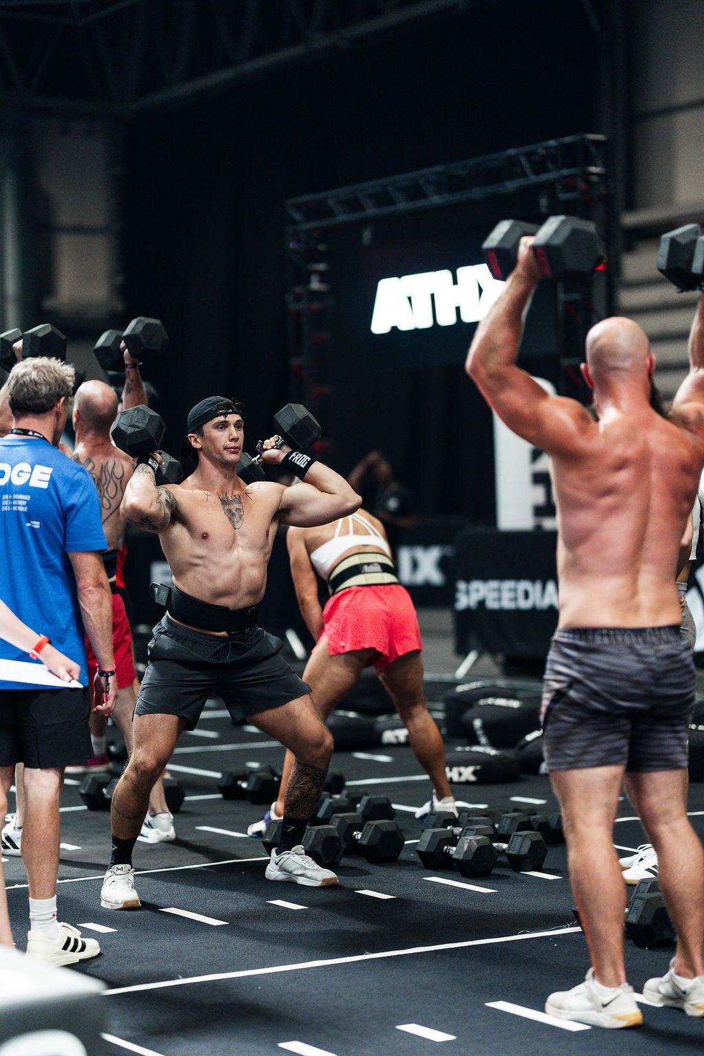 A full heat of athletes lifts dumbbells overhead under the ATHX sign